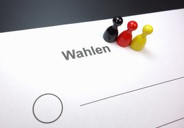 Symbolischer Wahlzettel mit drei Spielfiguren in den Farben schwarz, rot, gelb